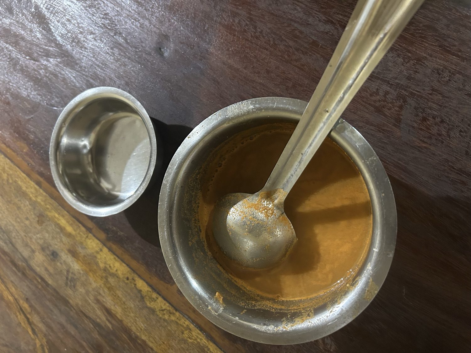 Paale kashaya — the bitter Aati Amavasya decoction — golden-brown in a steel bowl with a ladle and a small serving cup, on a dark wooden table